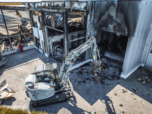 Bagger vor einer teilweise geöffneten Gewerbehalle