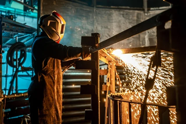 Mitarbeiter in Schutzausrüstung beim Trennen eines Metallbauteils